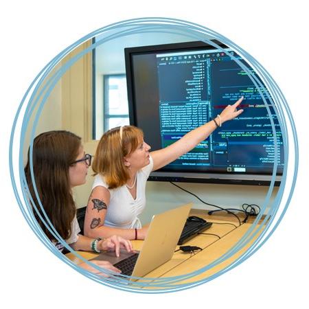 Two students review computer programming code on a large monitor